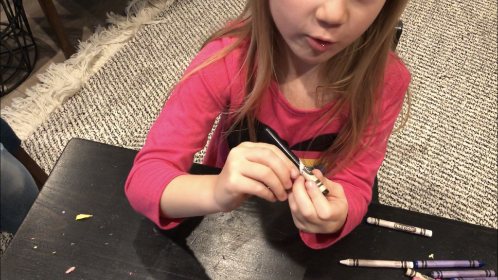 A little girl peeling the paper off of old crayons