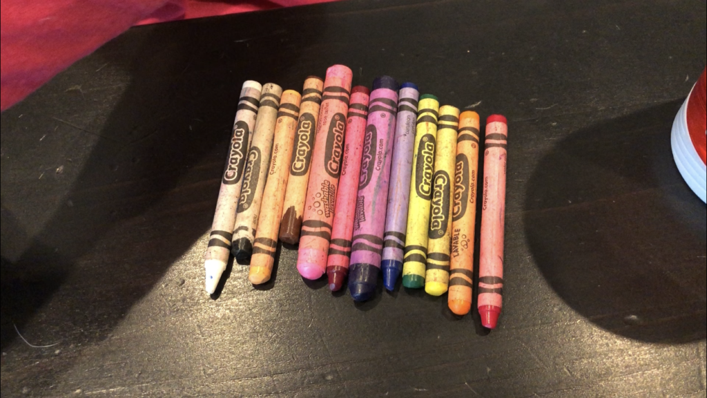 Old crayons creating a rainbow; white, black, peach, brown, light pink, fuchsia, purple, blue, green, yellow, orange, red