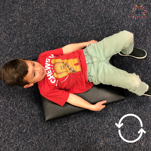 Child laying on his back (supine) to rotate himself 360 degrees on a scooter board