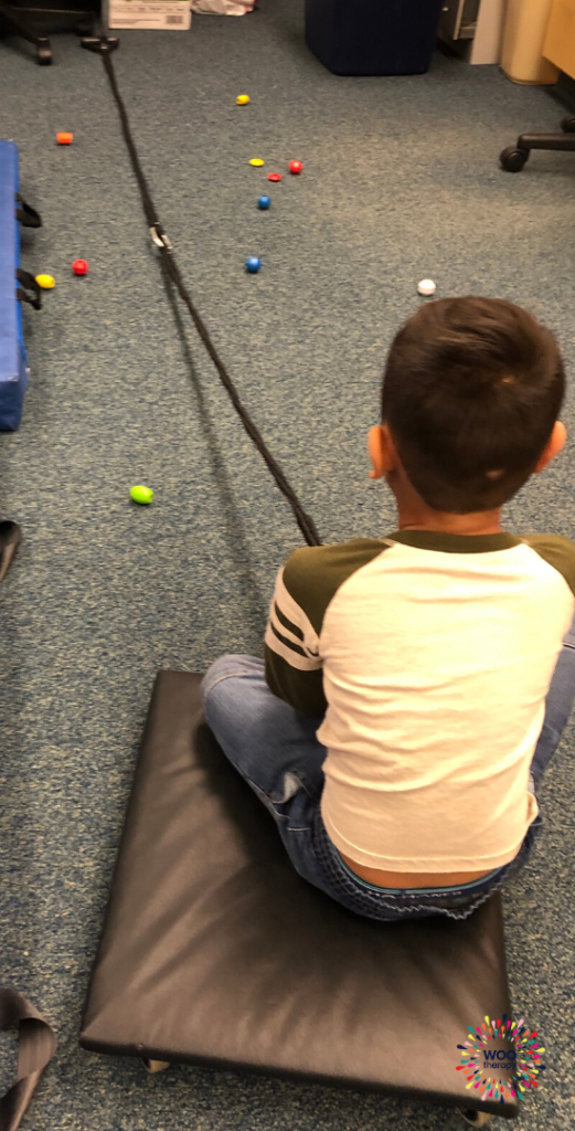 A boy seated on a scooter board pulling a rope.