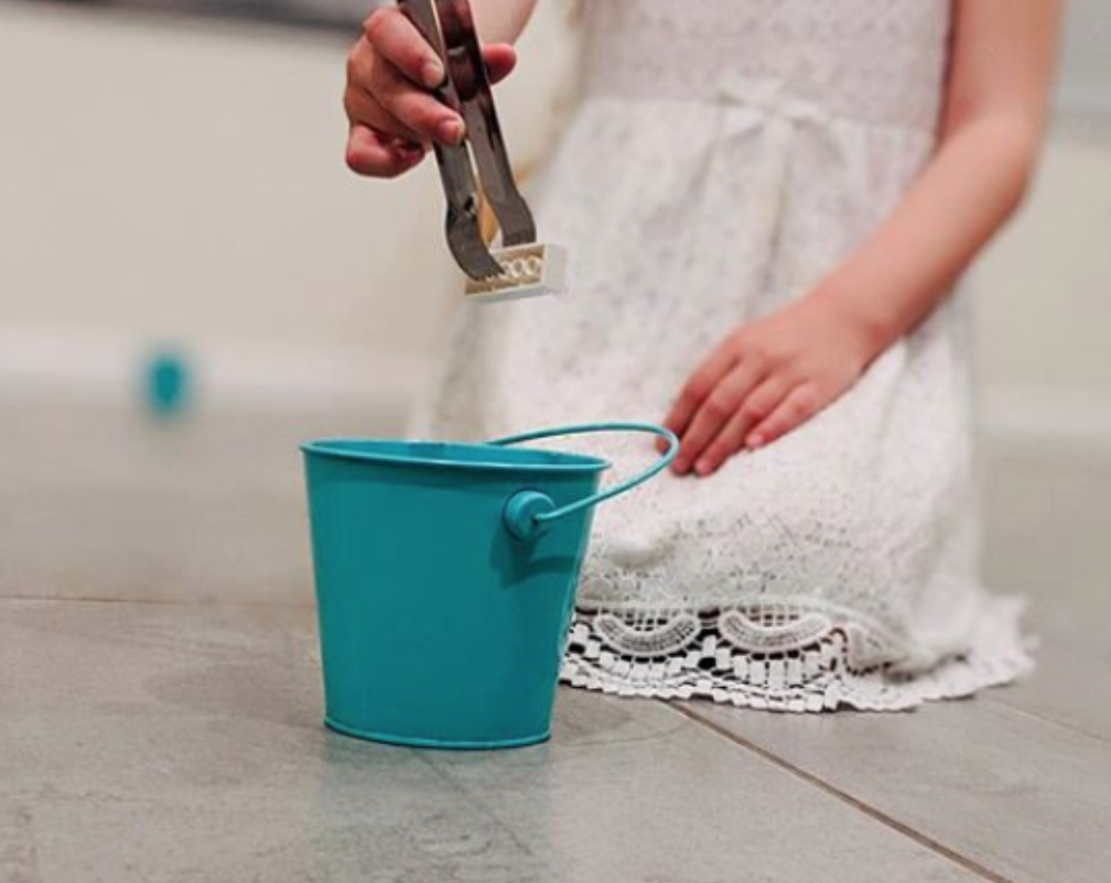 Using tongs to transfer small items to a bucket.