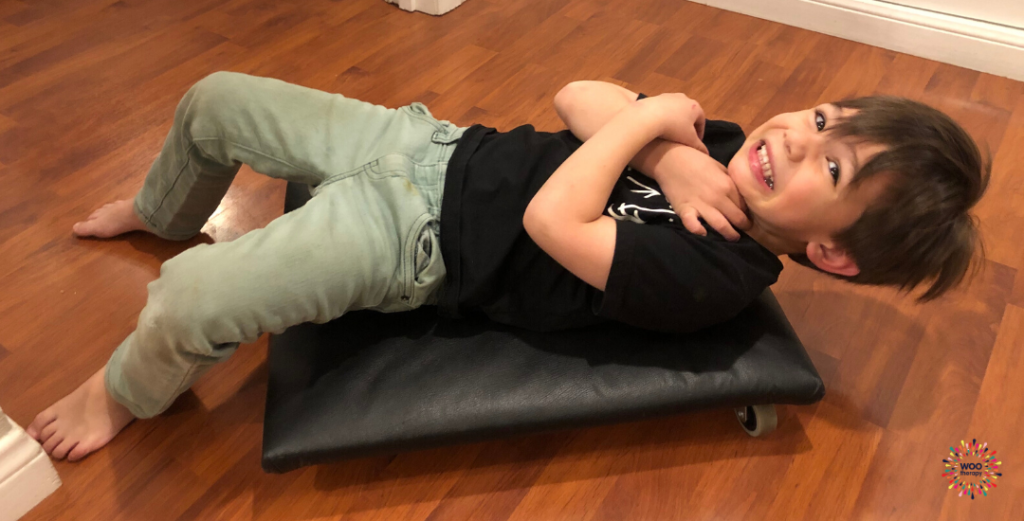 A boy on his back maintaining co-contraction and preparing to motor a scooter board with his feet.